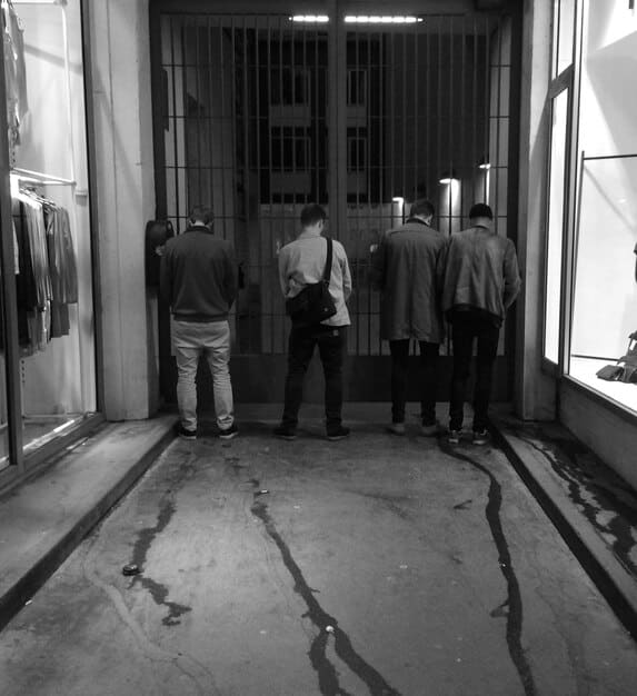 A black and white photo depicting a group of men in suits huddled together, exchanging money discreetly in the corridors of a government building, representing historical lobbying corruption.