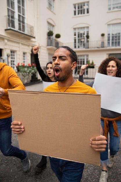 A diverse group of people holding protest signs and marching during a political rally, with some individuals holding smartphones and recording the event, reflecting the impact of citizen activism and social media in political movements.